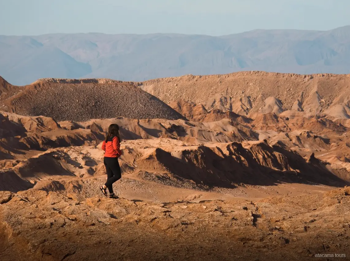 Atacama tours naar Baltinache, wandelaar in rode jas kijkt uit over geërodeerde woestijnruggen
