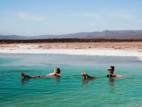 Passeios no Atacama, dois visitantes flutuando numa laguna salgada turquesa com montanhas ao fundo