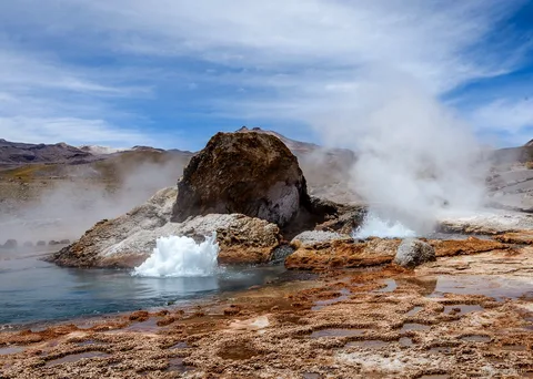 Atacama tours to El Tatio, a geyser bubbling beside a large boulder with steam and mineral terraces