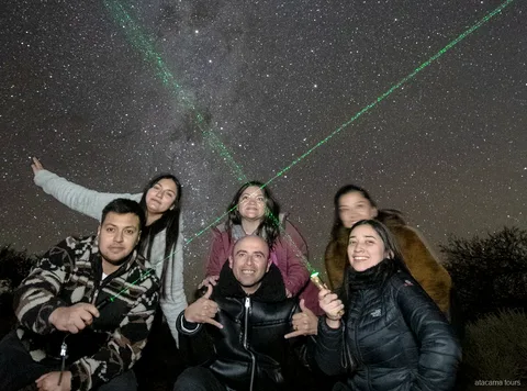 アタカマ星空ツアー、サンペドロ・デ・アタカマ近郊、緑色のレーザーポインターで星を指す天の川が見える夜空の下、笑顔で記念撮影するグループ