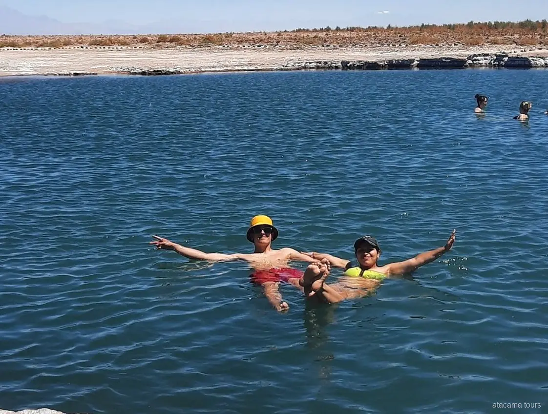 Atacama tours at Laguna Cejar, two visitors floating with arms outstretched in the salty blue lagoon
