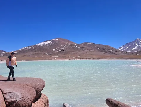 Atacama tours naar Piedras Rojas, bezoeker op rode rotsen naast een turquoise lagune en besneeuwde toppen