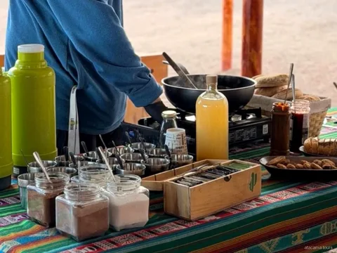 Atacama tours snack table with thermoses, jars, bread and a camp stove on a striped Andean tablecloth