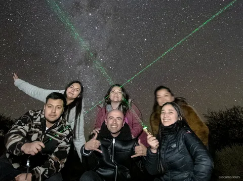 Tour astronomici ad Atacama, gruppo sorridente in posa sotto il cielo notturno con laser verdi