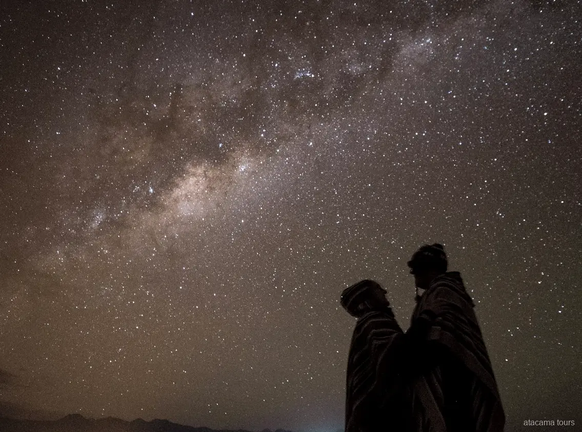 Tours astronomiques dans l'Atacama, deux silhouettes en ponchos sous la Voie lactée scintillante
