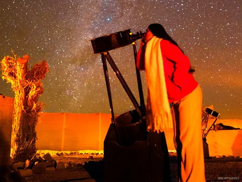 Tour ad Atacama, viaggiatrice che guarda in un grande telescopio sotto il cielo stellato del deserto