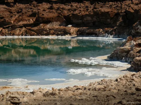 Tours en Atacama a Baltinache, laguna verde azulada bordeada de costra de sal blanca y rocas pardas
