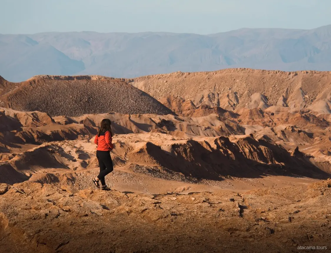 Passeios no Atacama a Baltinache, caminhante de jaqueta vermelha diante de cristas erodidas do deserto