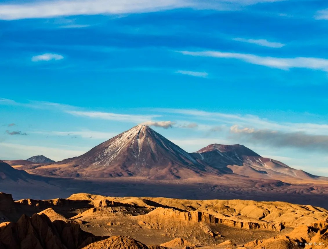 Paisaje de los tours en Atacama, cono volcánico con nieve sobre crestas doradas y erosionadas del desierto