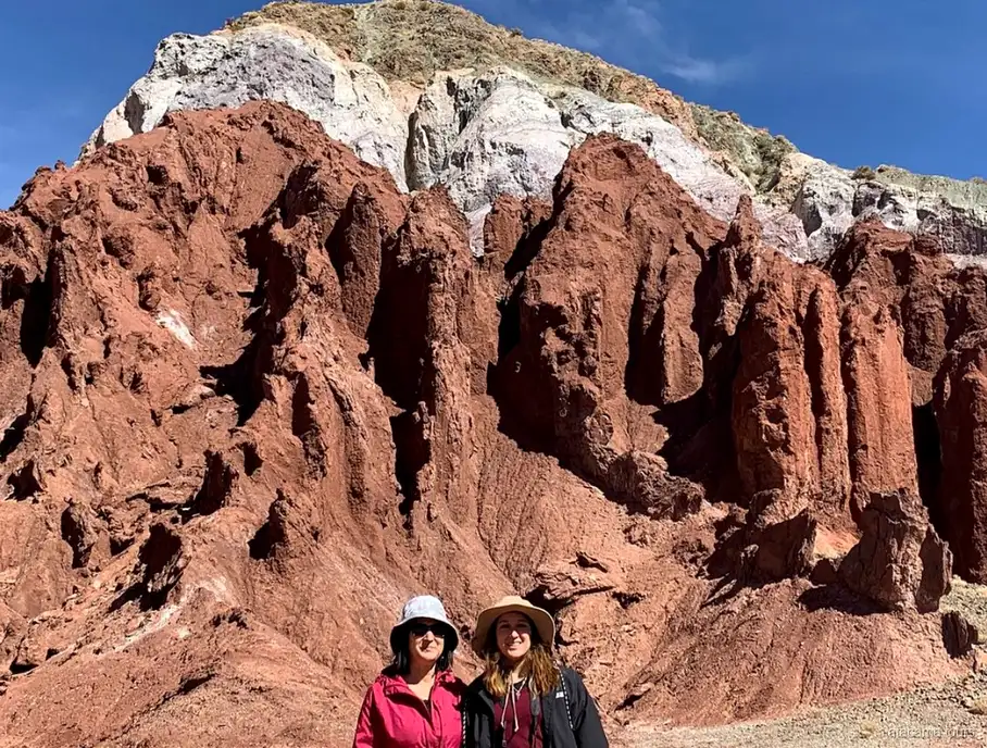 Tour nel deserto di Atacama alla Valle dell'Arcobaleno, due visitatori con cappello davanti a guglie di roccia rossa