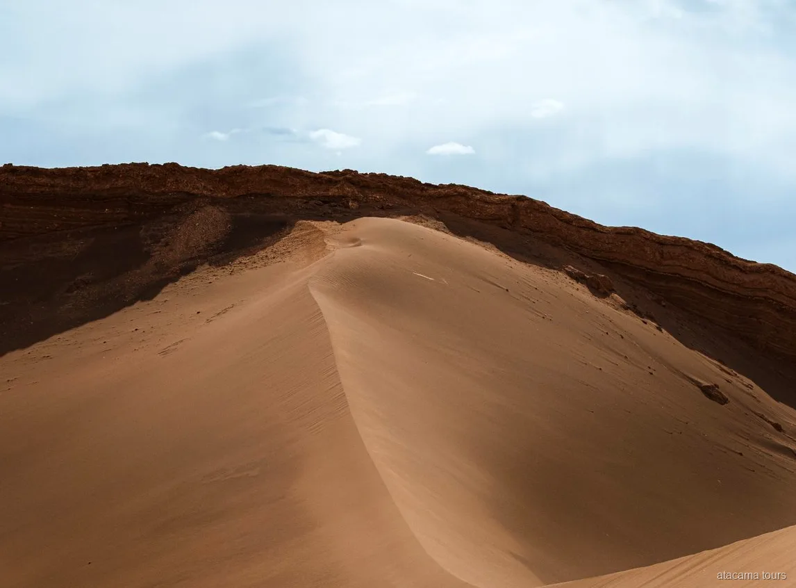 Tour nel deserto di Atacama al Valle de la Luna, duna di sabbia liscia sotto una cresta di roccia scura