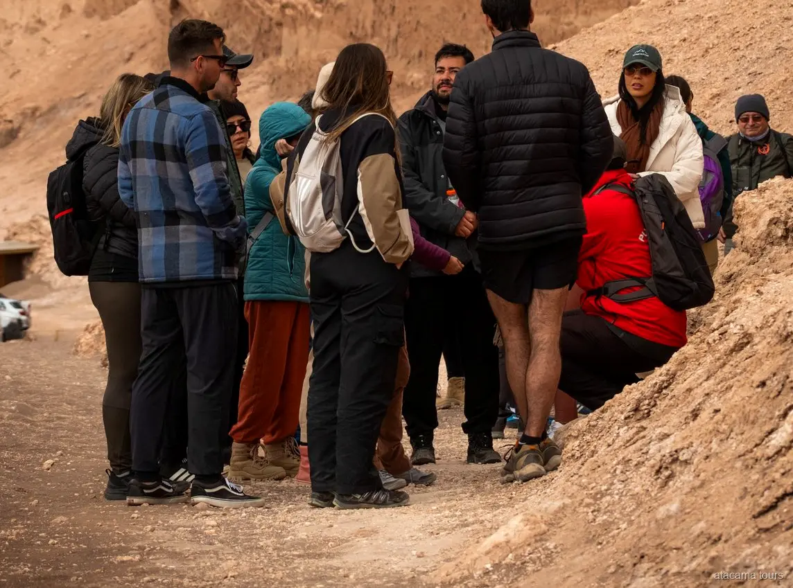 Grupo de tours en Atacama con chaquetas de abrigo reunido junto a su guía en un sendero del Valle de la Luna