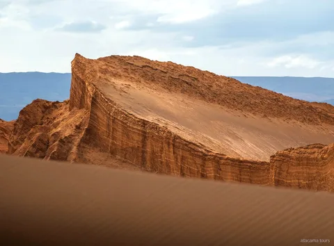 Atacama tours in de Valle de la Luna, schuin gelaagde rotswand boven een geribbelde zandduin